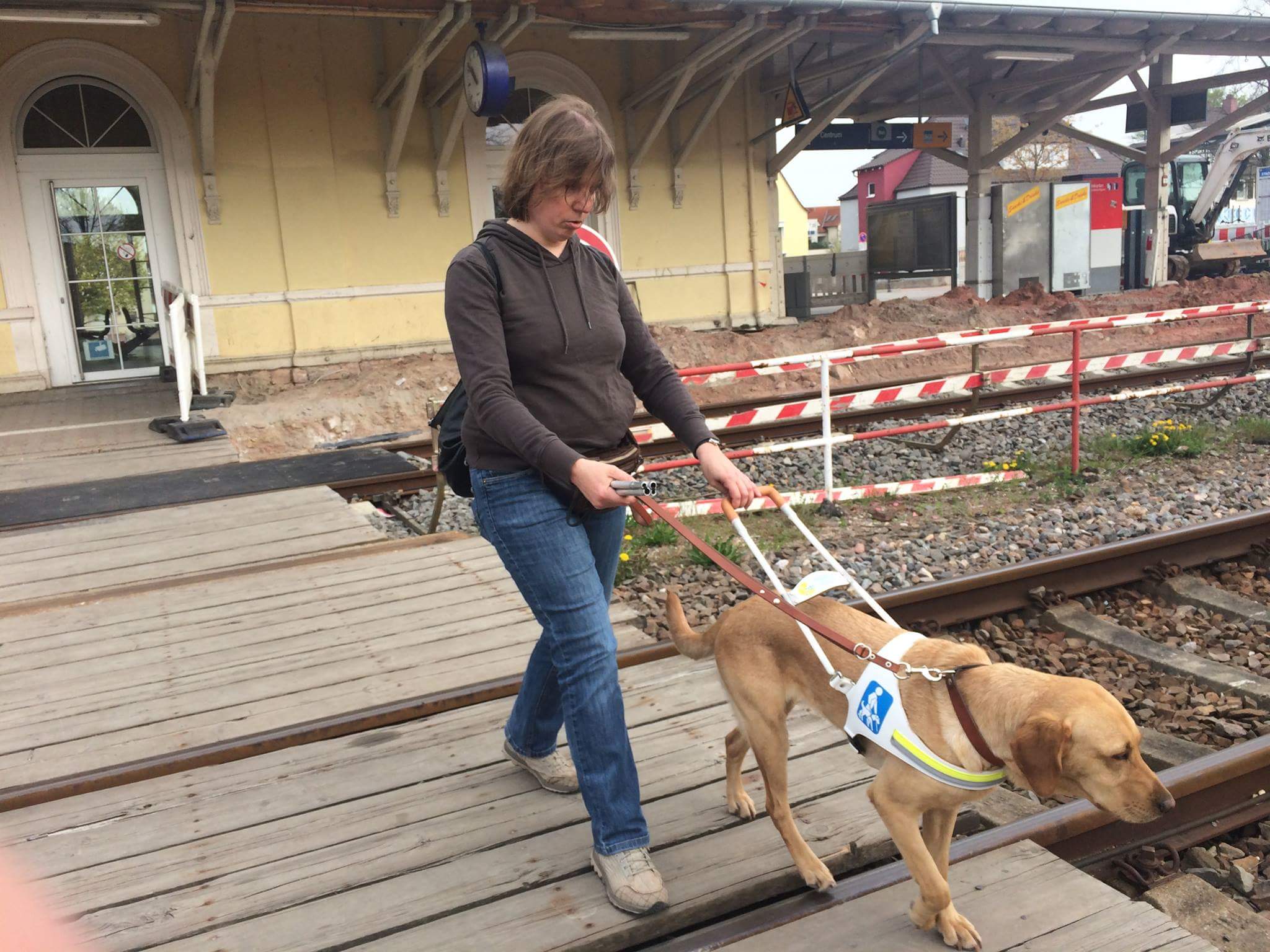 Frau geht mit Blindenhund über Bahnübergang